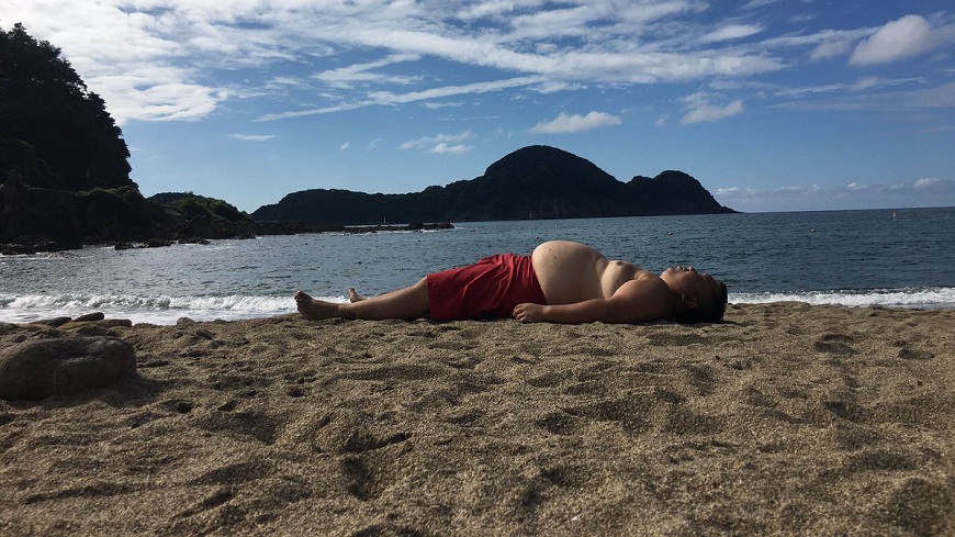 這位大肚男躺在沙灘上和後方的山勢做對照，網友全笑翻了。(圖／翻攝自推特)