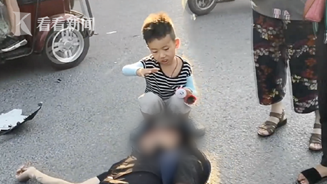 揚州日前發生一起車禍，一名7歲小男童蹲在傷者頭部附近幫忙遮太陽。(圖／翻攝自看看新聞) 