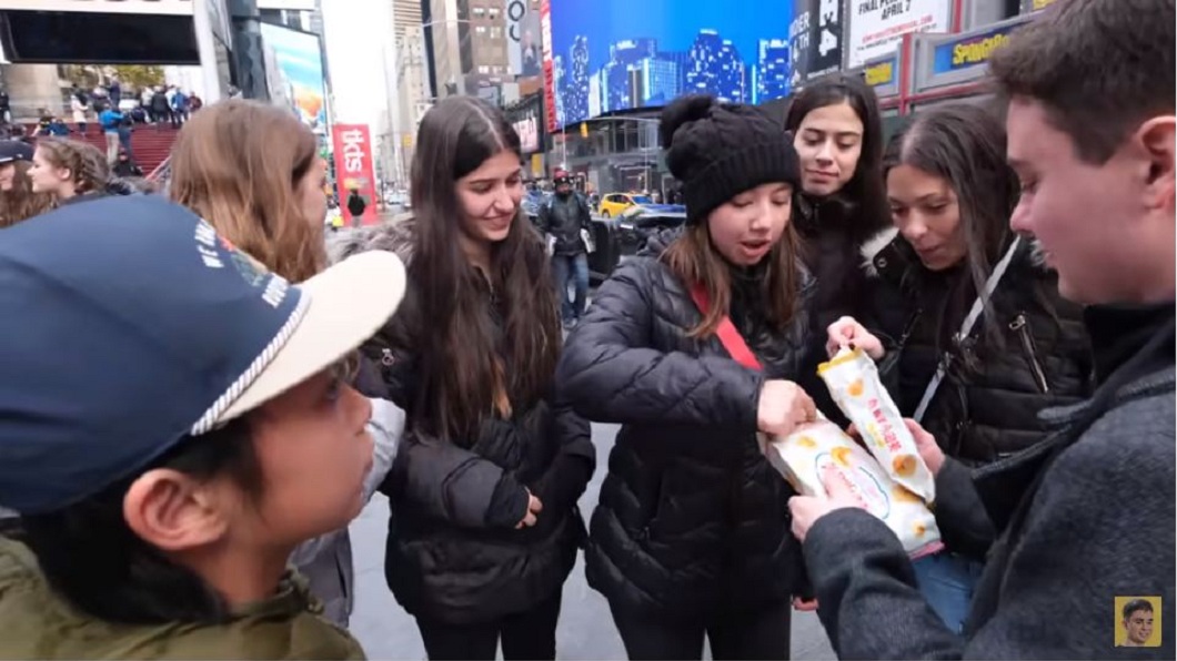美國YouTuber小馬拿著台灣常見的零食「義美小泡芙」，在紐約街頭供路人試吃。(圖／翻攝自YouTube)