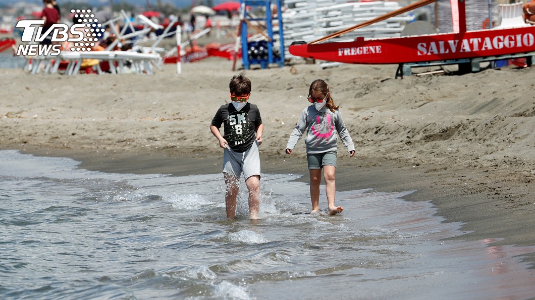 義大利封鎖後，首次正式重新開放後，戴著口罩的孩子們在海灘岸邊散步。（圖／達志影像路透社）