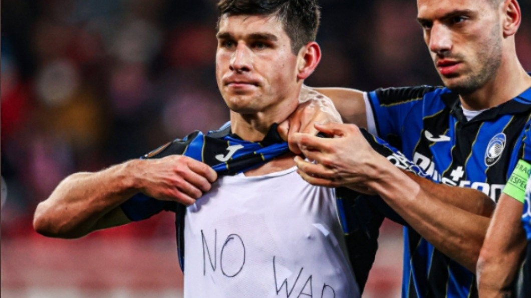 足球球員馬連洛夫斯基對著鏡頭秀出白色內衣上黑筆手寫的「烏克蘭不要戰爭」，隊友紛紛上前與他擁抱打氣。（圖／翻攝自推特）