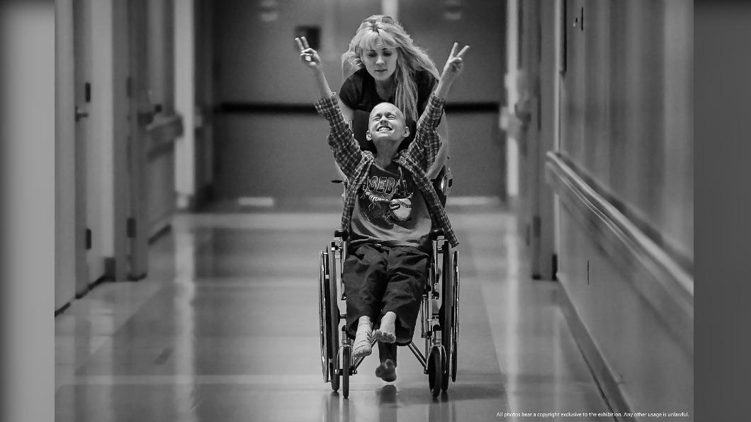 10歲德瑞克（Derek）儘管罹患癌症，仍在媽媽的鼓勵下樂觀抗病，這張在看診後雙手比YEAH的照片也因此獲得普立茲攝影獎殊榮。（圖／普立茲新聞攝影獎80週年展）