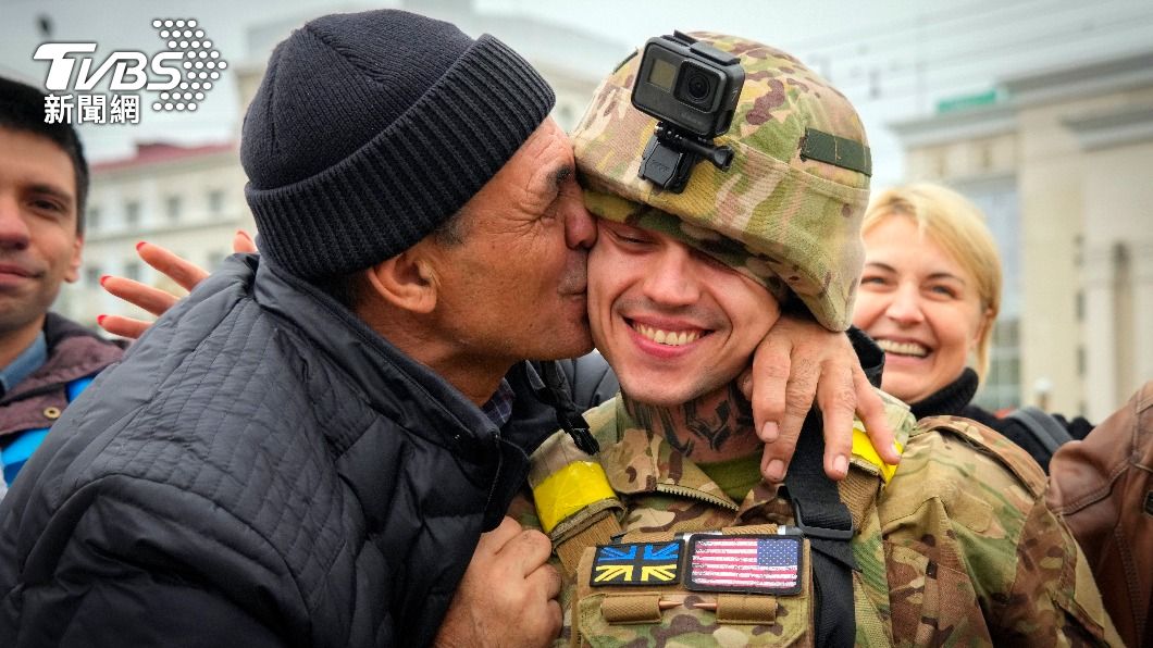 一名赫爾松大叔熱吻烏克蘭士兵，後方的圍觀群眾更露出看好戲的表情。（圖／達志影像美聯社）