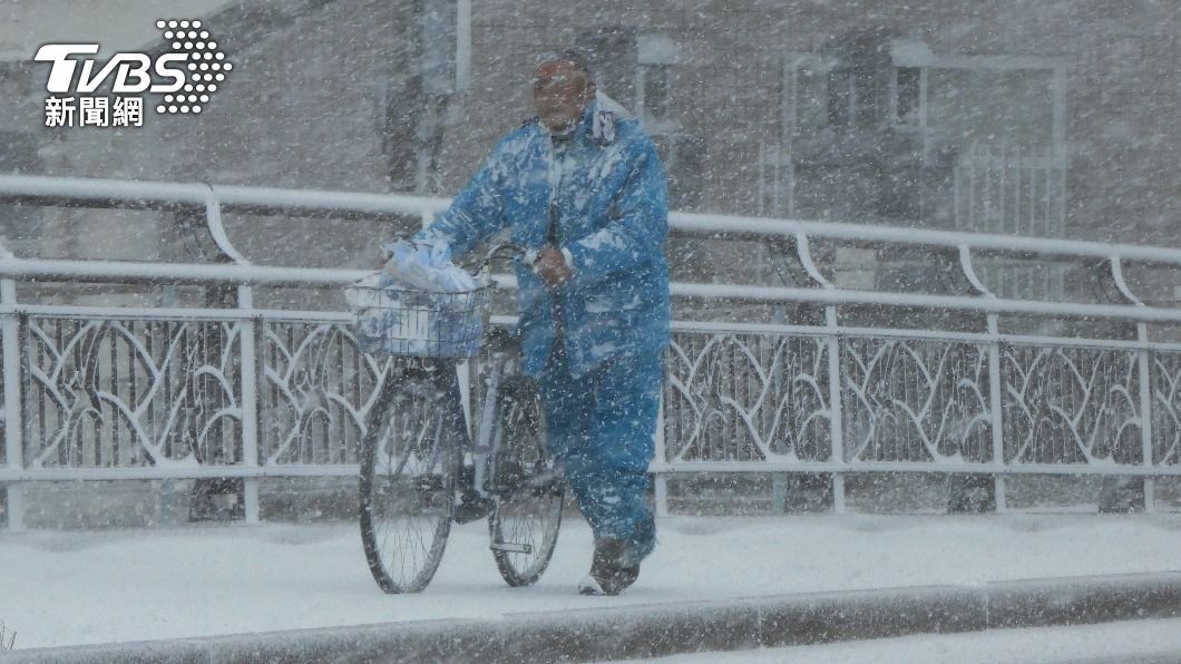 日本九州福岡縣今日下起大雪，一名居民在雪中顫抖著推動腳踏車。（圖／達志影像美聯社）