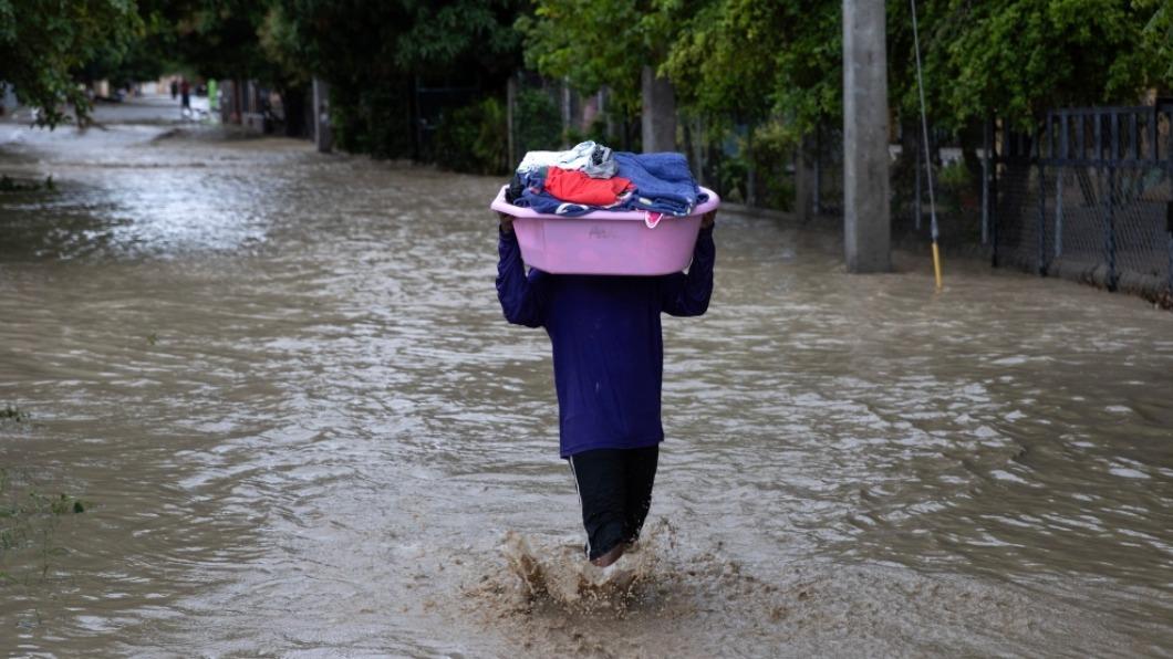 多明尼加水患造成21人死亡，1萬多人被迫遷移，圖為民眾拿著個人物品，困難前行。（圖／翻攝自@EPA_Images推特）